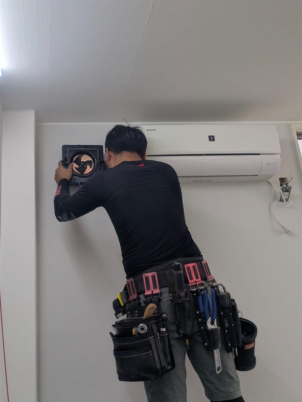施工中、職人が既設のエアコン横に換気ユニット本体を取り付けている様子
